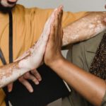 Good Deals - Crop smiling African American male with vitiligo skin giving high five to colleague in studio