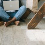 Discounted Stays - A Man Sitting on the Wooden Flooring while Looking at His Debit Card