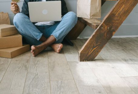 Discounted Stays - A Man Sitting on the Wooden Flooring while Looking at His Debit Card