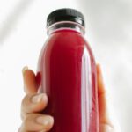 Detox Programs - Unrecognizable woman holding bottle of red juice against white wall