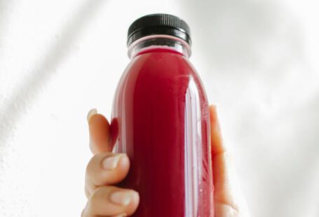 Detox Programs - Unrecognizable woman holding bottle of red juice against white wall