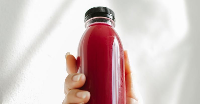 Detox Programs - Unrecognizable woman holding bottle of red juice against white wall